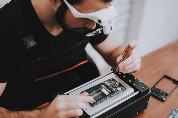 Young Man Repairing Hardware Equipment in Repair Shop. Worker with Tools. Computer Hardware. Electronic Devices Concept. Bearded Man. Modern Devices. Digital Device. Man in Glasses. - Fotoğraf, Görsel