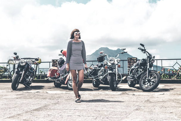 БАЛИ, ИНДОНЕЗИЯ - 12 августа 2018 года: Женщина на фоне мотоциклов Harley Davidson, вулкан Батур
. - Фото, изображение