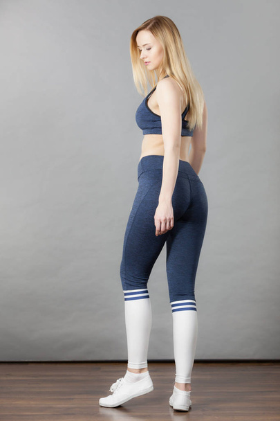 Woman wearing sporty workout outfit, blue sport bra, leggings, socks and trainers. Indoor shot on grey background. - Φωτογραφία, εικόνα