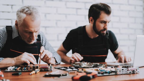 Two Men Repairing Hardware Equipment from PC. Repair Shop. Worker with Tools. Computer Hardware. Young and Old Workers. Modern Devices. Digital Device. Laptop on Desk. Electronic Devices Concept. - Фото, изображение