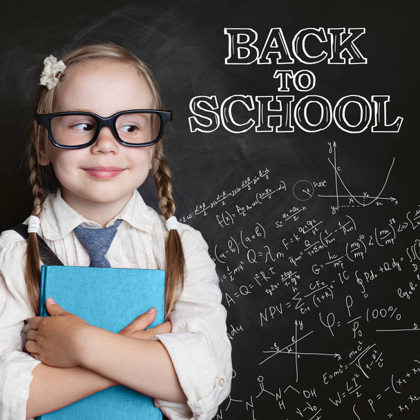 Back to school concept. Cute little girl in glasses on chalk board background - Photo, Image