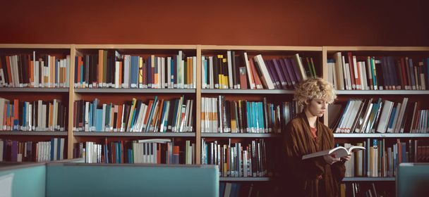 νεαρή γυναίκα διαβάζει ένα βιβλίο στη βιβλιοθήκη - Φωτογραφία, εικόνα