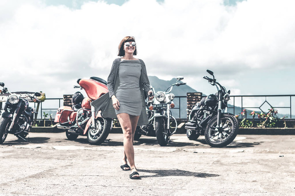 BALI, INDONÉSIA - AGOSTO 12, 2018: Mulher no fundo das motocicletas Harley Davidson, vulcão Batur
. - Foto, Imagem