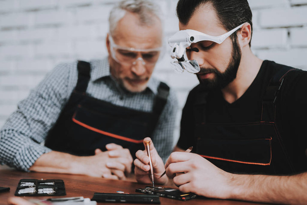 Two Men Repairing Hardware Equipment in Workshop. Repair Shop. Young and Old Workers. Digital Device. Man in Glasses. Electronic Devices Concept. Mobile Device Hardware. Workers with Tools. - Foto, Imagem