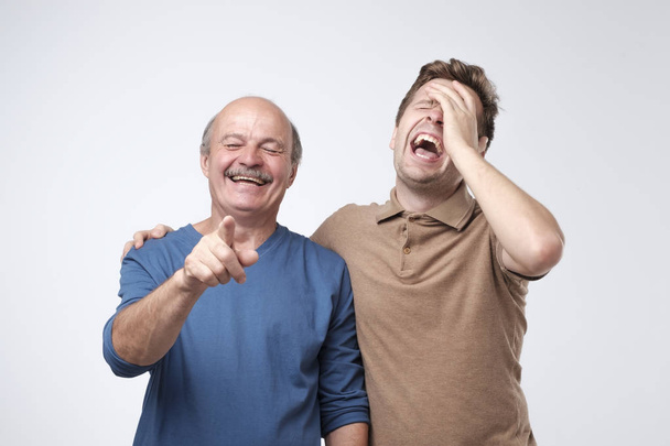 Two friends in casual colorful wear standing and laughing together. Mature son and father together chortling . Two men having fun. - Photo, Image