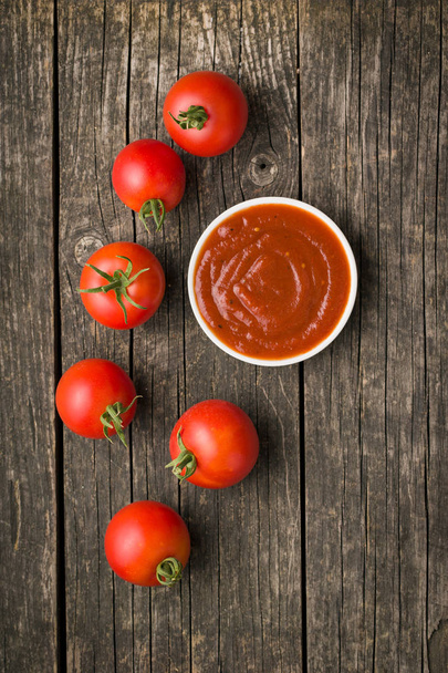 Tomatoes and ketchup on old wooden table. - Фото, изображение