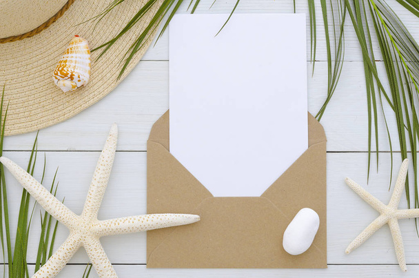 Beyaz ahşap zemin üzerinde kart şablonuyla mockup zarf. Tropikal palmiye yaprağı, yaz şapka, seastars ve kabuk. Daveti veya tebrik kartı kavramı - Fotoğraf, Görsel