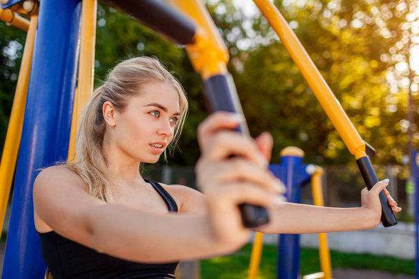 Fiatal nő képzés gép sportsground nyáron. Dolgozik a bicepsz izmok. Sportos életmód - Fotó, kép