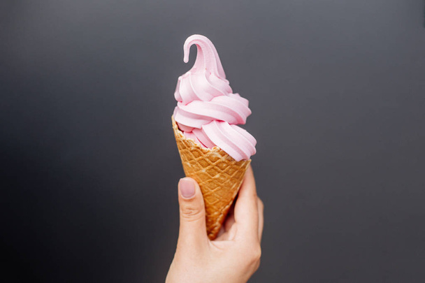 Pink ice cream in the hand near gray wall. - Foto, afbeelding
