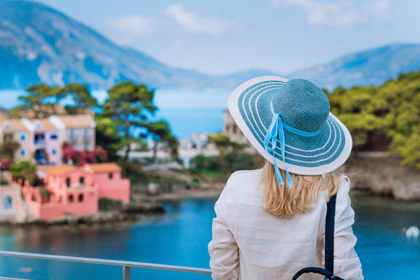 Tourist woman in blue sunhat on view point platform admire view of colorful tranquil village Assos on sunny day. Enjoying visiting Kefalonia on Greece summer travel vacation - Foto, imagen