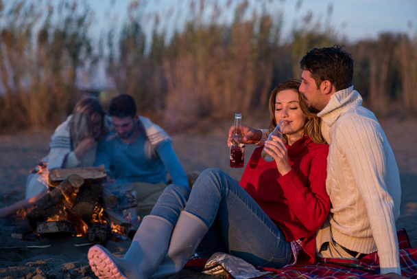 Young Couple enjoying with friends Around Campfire on The Beach At sunset drinking beer - Foto, Bild