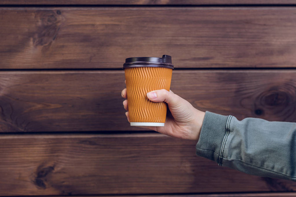 コーヒーが大好き茶色の木製の背景の前にコーヒーのカップを持っている人の手 - 写真・画像