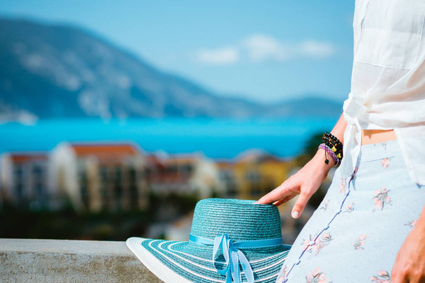 Blue sunhat laying on the wall. Tourist woman enjoying view of colorful tranquil village Assos on sunny day. Stylish female visiting Kefalonia in summer time on Greece travel vacation - Foto, Bild
