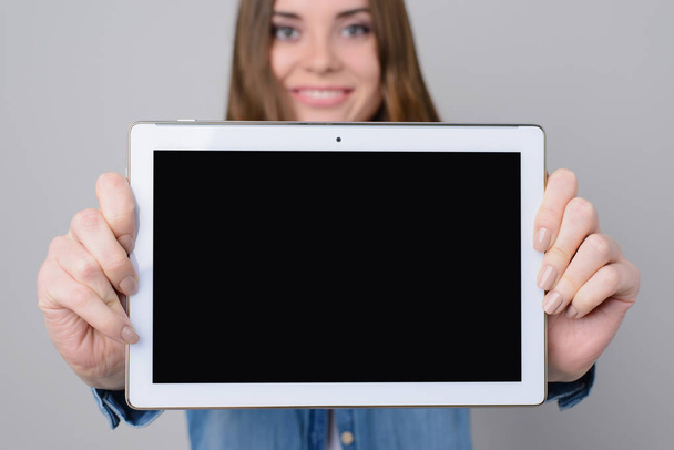 Woman with beautiful face, toothy smile is showing digital tablet with empty black screen. Close up photo, isolated on grey background - Foto, Imagem