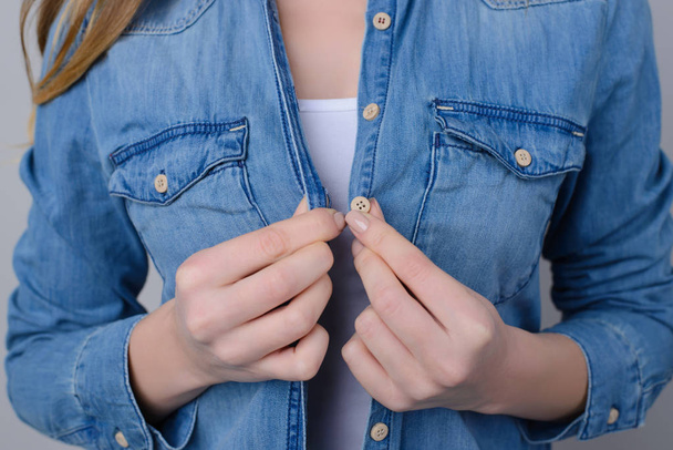 Concept de magasinage de vêtements. Photo recadrée d'une femme essayant de fixer le bouton sur sa chemise en jean ou de le déboutonner
. - Photo, image