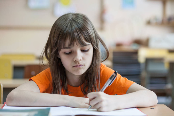 Маленькая девочка пишет что-то в блокноте и сидит за столом - Фото, изображение