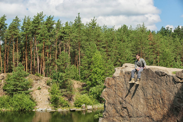 Jongeman op rots in de buurt van meer en bos. Camping seizoen - Foto, afbeelding