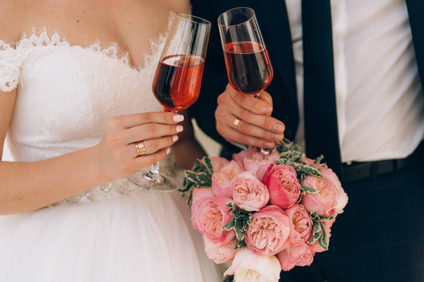 Nahaufnahme des zugeschnittenen Rahmens, das Ehepaar hat gerade geheiratet, hält ein Glas rosa Champagner in der Hand, feiert ihre Hochzeit, das Mädchen hält ihren Brautstrauß, - Foto, Bild