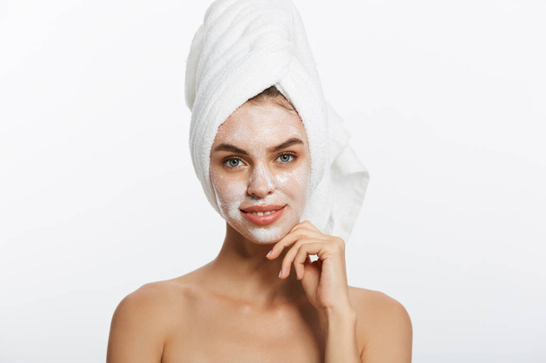Atraktivní mladá žena vnořen do osušky, používání krému na její tvář po sprcha v koupelně. - Fotografie, Obrázek