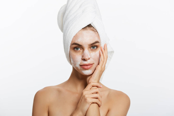 Aantrekkelijke jonge vrouw omwikkeld met badhanddoeken, toe te passen crème op haar gezicht na een douche op de badkamer - Foto, afbeelding