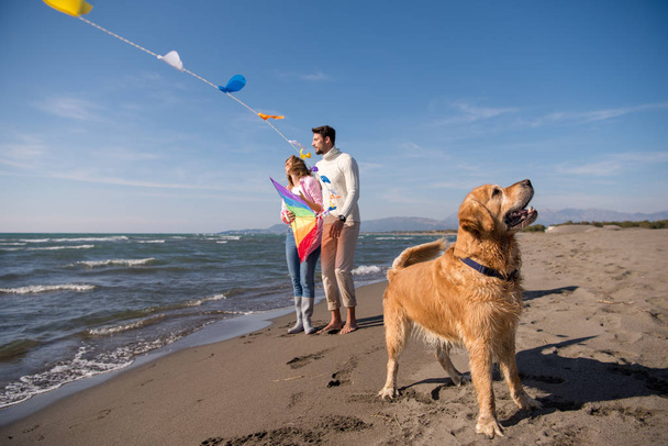 Young Couple having fun playing with a dog and Kite on the beach at autumn day - Foto, imagen