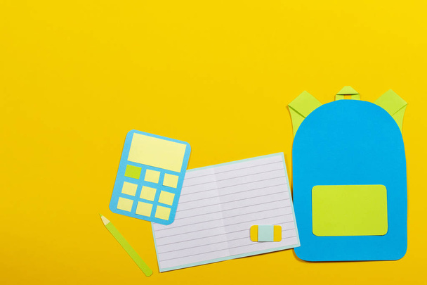 Schulbildung papiergeschnittener Hintergrund. Schulranzen-Rucksack, Notizbücher und Taschenrechner auf gelbem Hintergrund - Foto, Bild