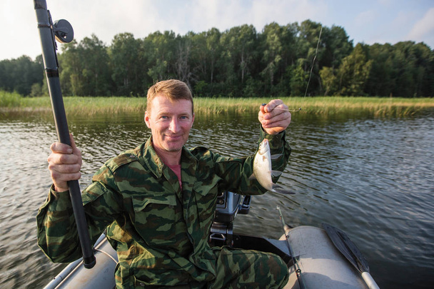 Pescador em camuflagem em um barco de borracha no lago
. - Foto, Imagem