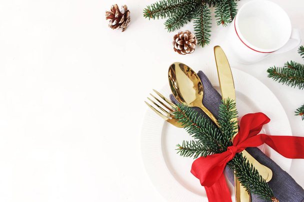 Traditional Christmas table place setting. Golden cutlery, linen napkin, spruce branches and cup of milk. Pine cone and red ribbon decoration. Holidays background. Flat lay, top view with copy space. - Foto, Bild