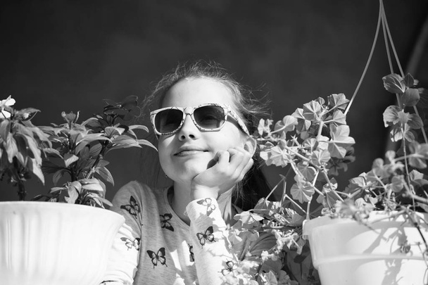 Small girl with flowers. Fashion child wear sunglasses on sunny day. Beauty kid with plant pots in summer or spring. Freshness and youth concept - Foto, afbeelding
