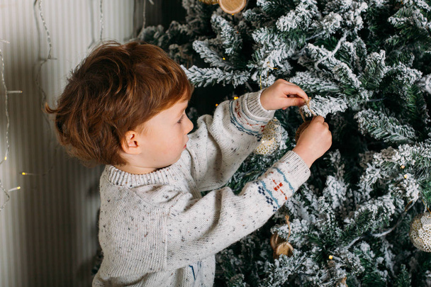 Cute little kid decorating Christmas tree with red beads - Φωτογραφία, εικόνα