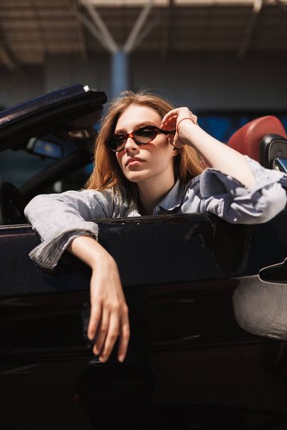 Menina bonita em óculos de sol no carro cabriolet pensativo olhando para o lado passar o tempo ao ar livre
 - Foto, Imagem