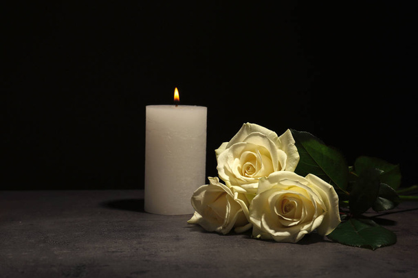 Beautiful white roses and candle on table against black background. Funeral symbol - Foto, Imagen