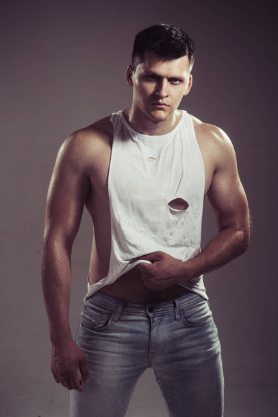 Man in sexy tank top and jeans on grey background. Man with muscular hands with biceps and triceps - Fotoğraf, Görsel