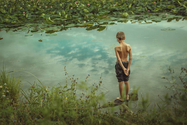 Niño pensativo con gafas en un lago con lotos
 - Foto, imagen