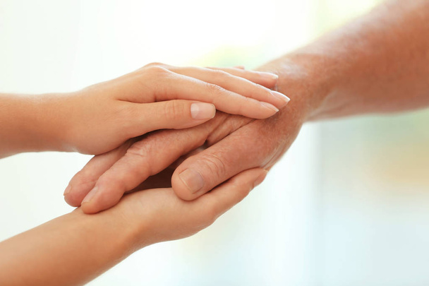 Young woman holding elderly man hand on blurred background, closeup. Help service - Foto, Imagen
