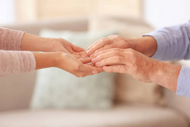 Young woman holding elderly man hands indoors, closeup. Help service - Foto, Imagen
