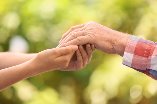 Young woman holding elderly man hand on blurred background, closeup. Help service - Photo, Image