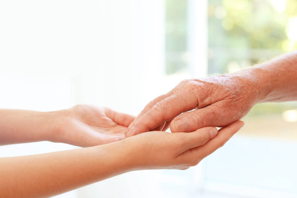 Pomaganie dłoniom na rozmytym tle, zbliżenie. Koncepcja opieki nad osobami starszymi - Zdjęcie, obraz