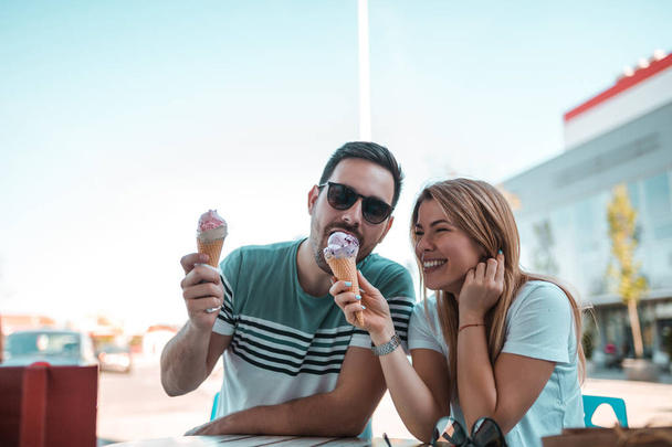 Good looking young man eating his girlfriends ice-cream while they sitting outdoors and having fun times - Фото, зображення