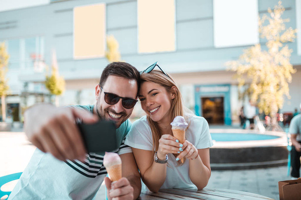 サングラスをかけた若い男が彼らは屋外アイス クリームをしながら、彼のガール フレンドと selfie を取っています。 - 写真・画像