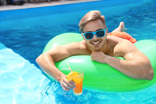 Young man with cocktail in pool on sunny day - Valokuva, kuva