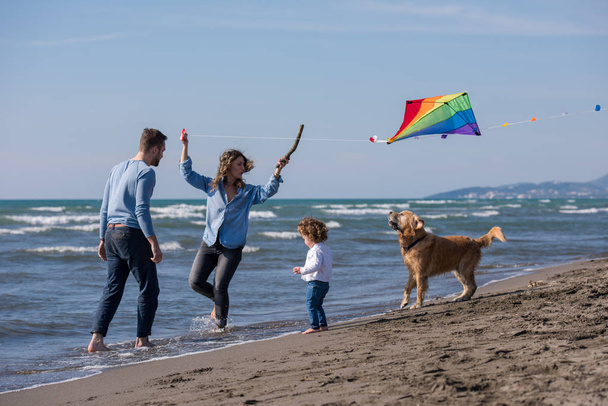 happy young family with kids having fun with a dog and  kite at beach during autumn day - Фото, зображення