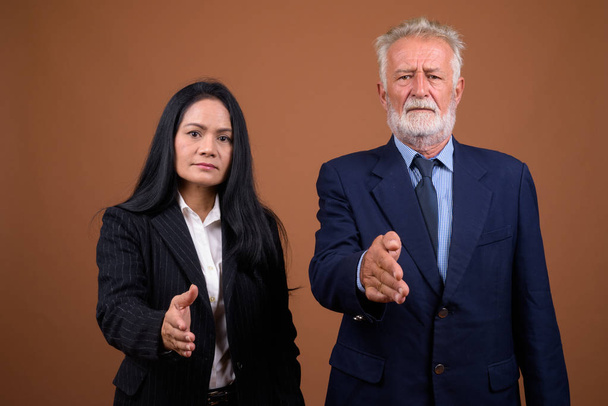 Mature multi-ethnic business couple against brown background - Photo, Image