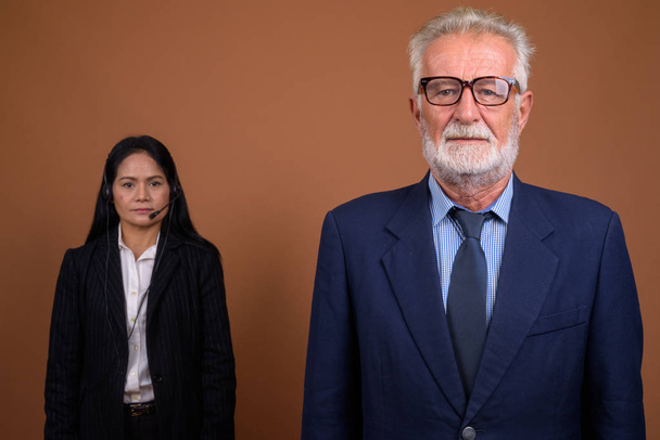 Reifes multiethnisches Businesspaar vor braunem Hintergrund - Foto, Bild