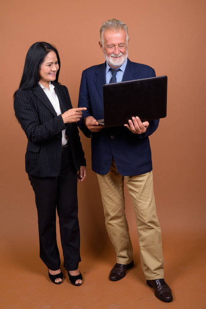 Mature multi-ethnic business couple against brown background - Foto, afbeelding
