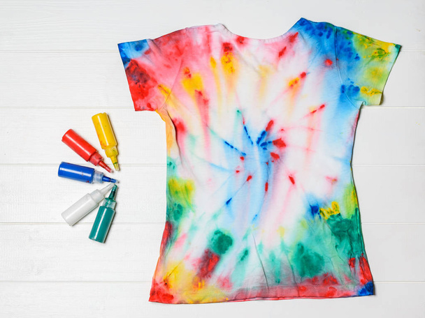 Tubes of paint for clothes and t-shirt in tie dye style on a white wooden table. White clothes painted by hand. Flat lay. - Photo, Image