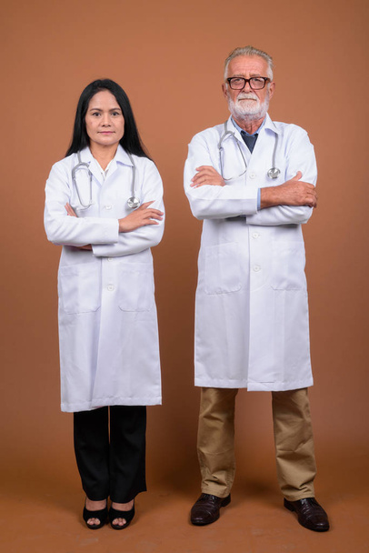 Mature multi-ethnic couple doctors against brown background - 写真・画像