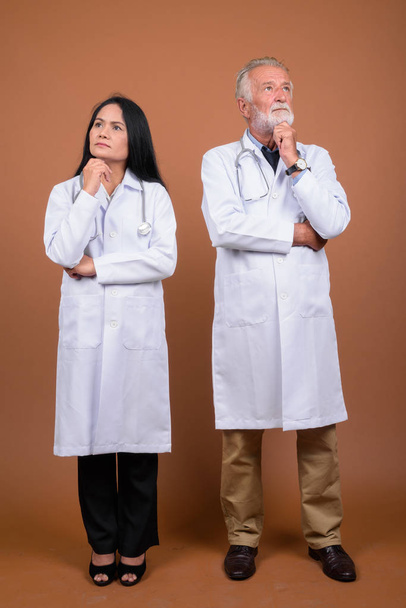 Mature multi-ethnic couple doctors against brown background - Photo, Image