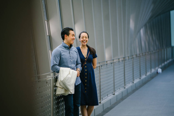 Portrait of an Asian Chinese couple on a date over the weekend. The man is young, handsome and well-dressed and the woman is wearing an elegant summer dress. They are  on a bridge. - Фото, зображення
