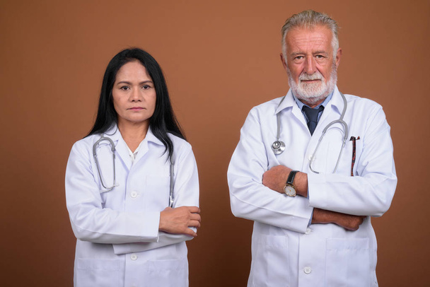 Mature multi-ethnic couple doctors against brown background - Foto, Imagen